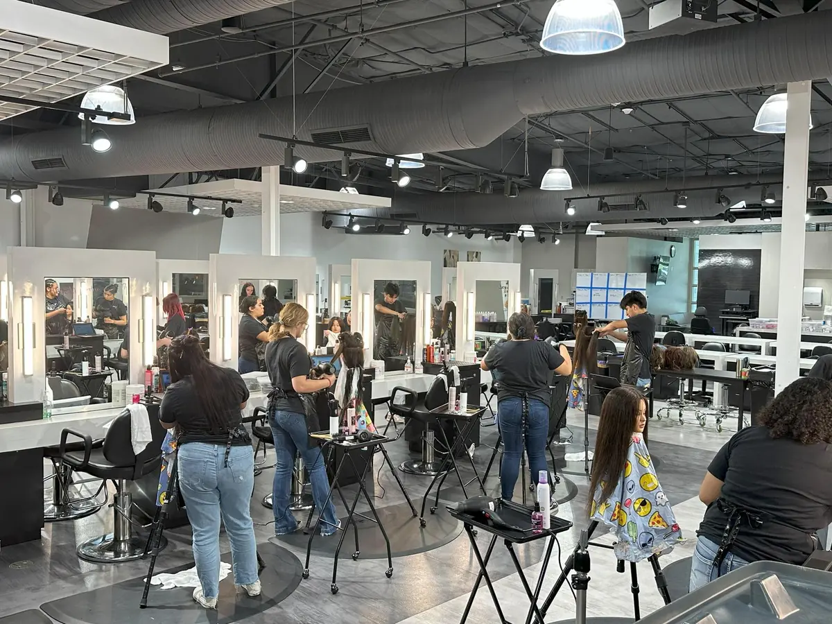 Wide cosmetology training salon at the Regional Occupational Center, with students styling clients' hair at mirrored workstations beneath industrial ceiling lights.