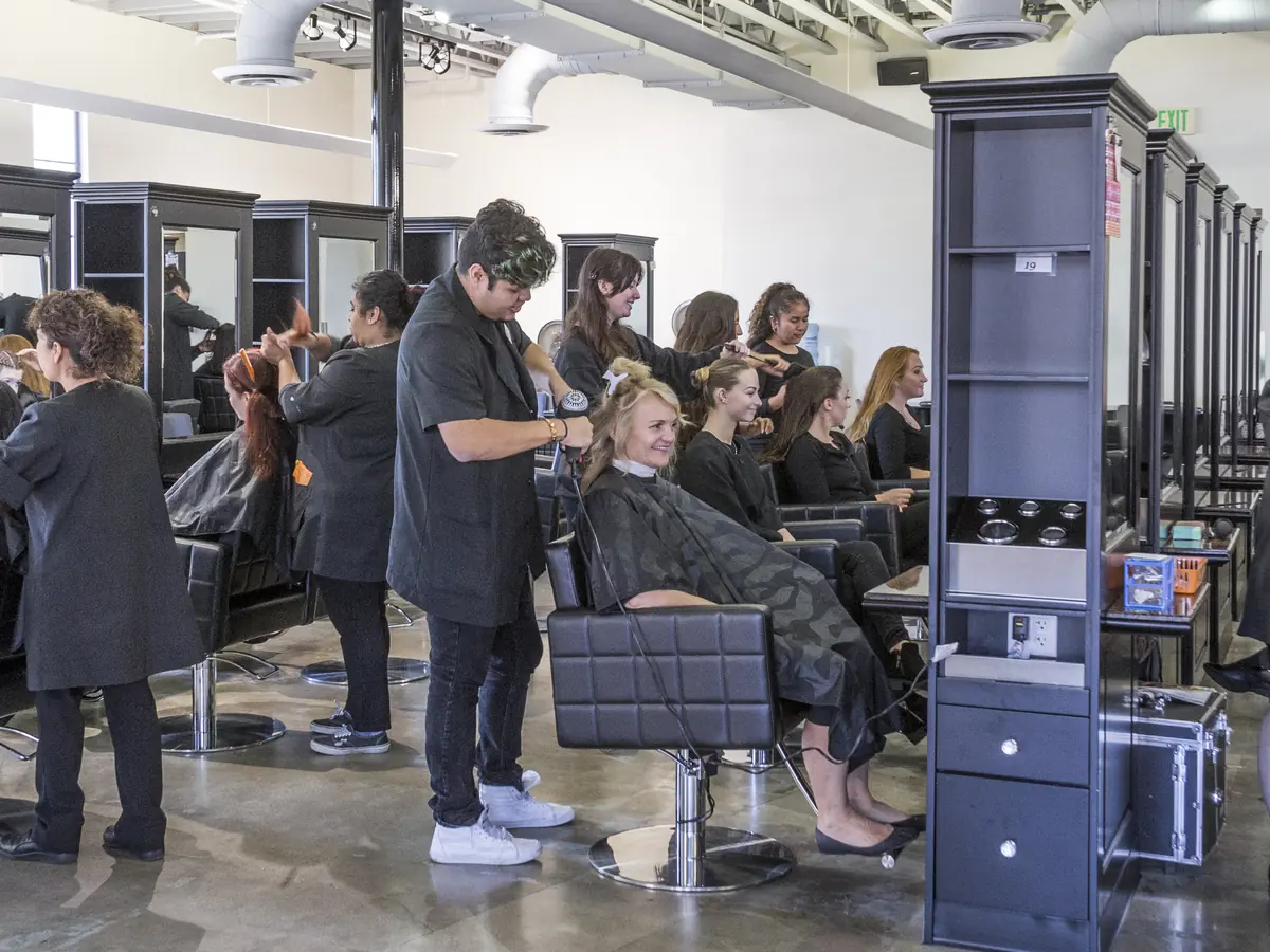 Students in a cosmetology training salon at Santa Barbara City College style clients seated at salon stations.