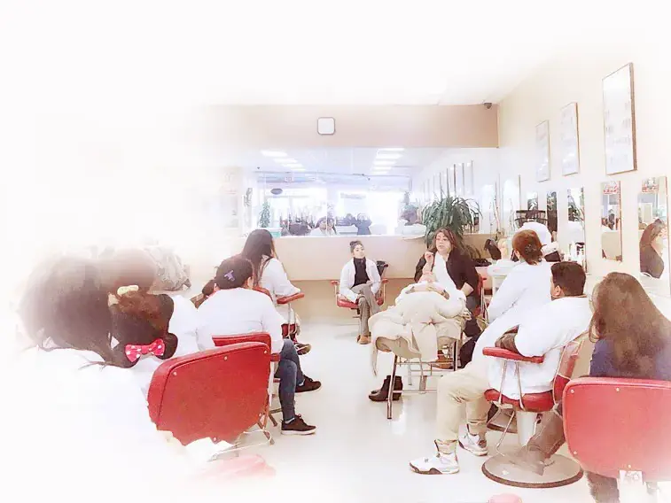 Interior of Santa Clara Beauty College showing students and clients seated in red salon chairs during beauty services in a bright classroom with mirrors along the walls.